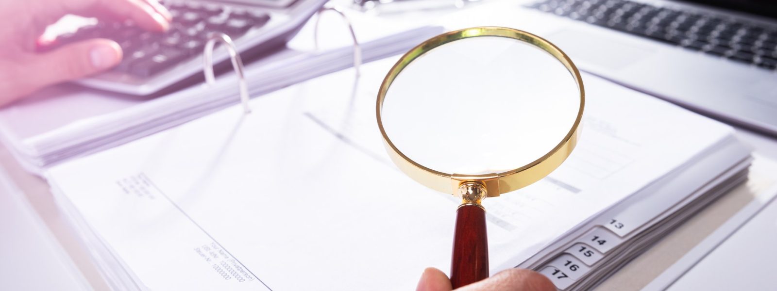 Close-up Of A Businessperson's Hand Analyzing Bill With Magnifying Glass In Office